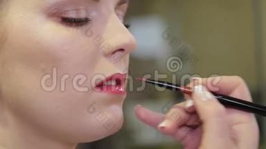 专业化妆师用刷子在客户的嘴唇上涂上唇彩。